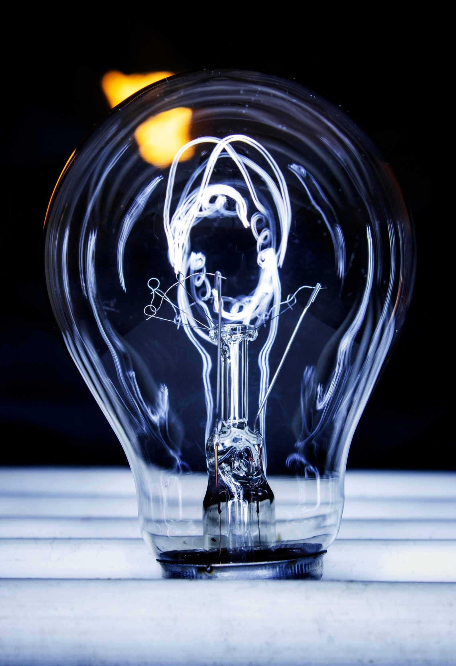 Artistic photo featuring a glowing light bulb with visible filament against a dark background.